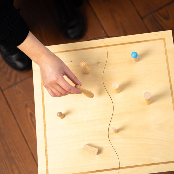 Draufblick auf ein Systembrett mit Figuren. Eine Hand platziert eine neue Figur.