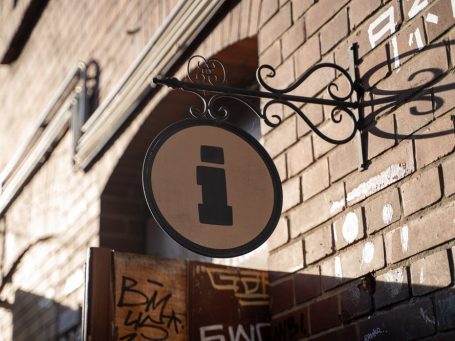 Runder Informationsschild an einer Ziegelmauer, mit braunem Hintergrund und schwarzem Symbol.